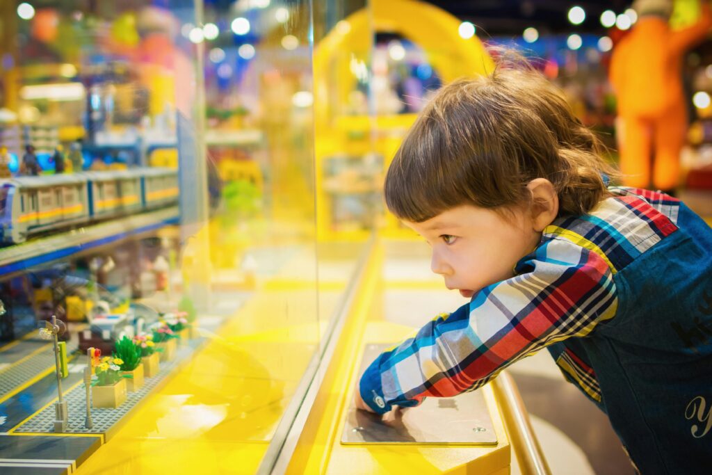 Home A young boy intently observes a colorful toy train display in a vibrant toy store.
