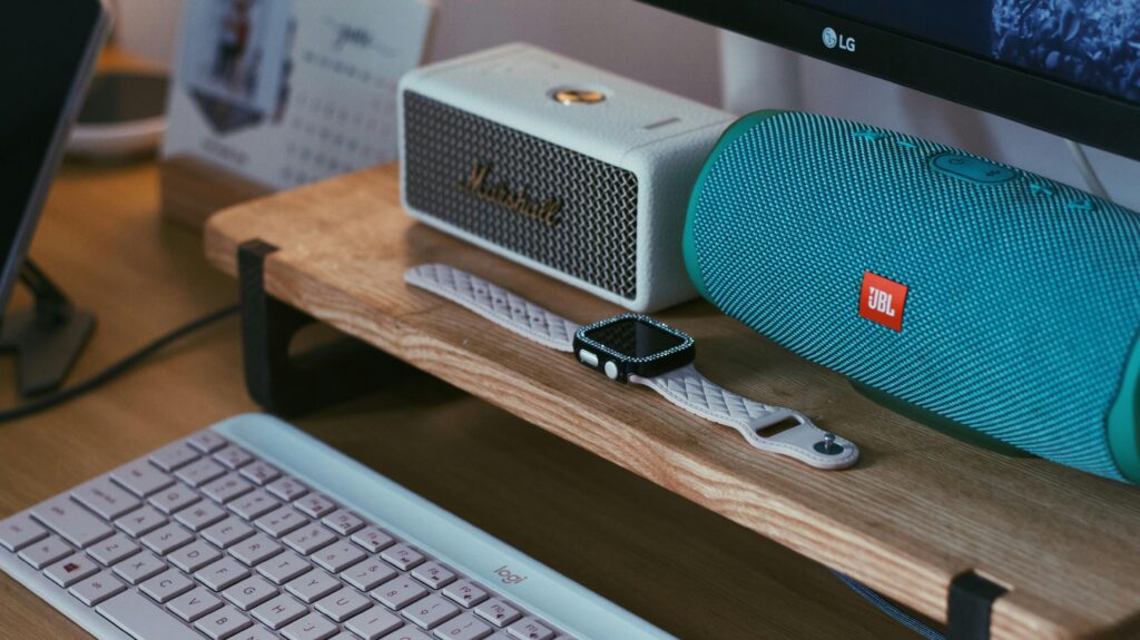Home A close-up of a modern workspace featuring Bluetooth speakers, a smartwatch, and a keyboard.